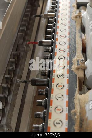 Industrial woodworking machine with multiple drill bits performing precise boring operations on a workpiece, creating sawdust and demonstrating a mode Stock Photo