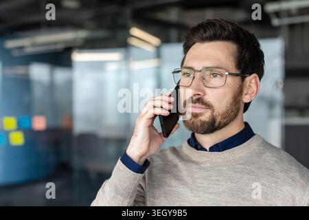 Serious male professional is having an important phone conversation, communicating and concentrating on a call while standing in a modern corporate office environment Stock Photo