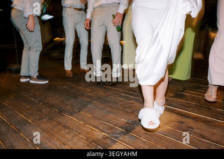 Wedding feet dancing. Close photographic shot of wedding feet in slippers during joyful dance on wooden planks Stock Photo