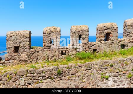 Rugged stone walls and crenellated battlements of medieval Molyvos Castle stand firm against a clear blue sky and the sparkling turquoise waters of th Stock Photo