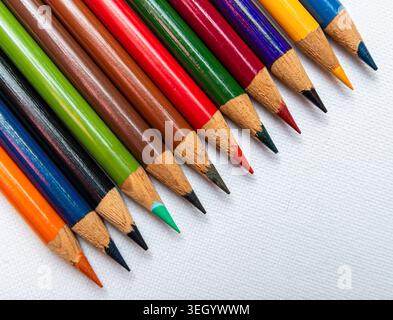 Colored pencils are lined up on a flat white surface with sharp tips visible. Each pencil has a different color and design. Stock Photo