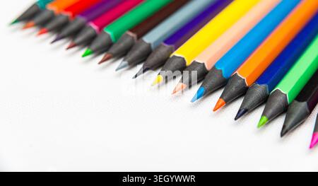 Pencils of various colors are lined up on a white surface. Each pencil shows its sharpened tip. They are ready for use in creative activities. Stock Photo