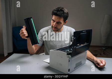 Male frustrated by printer problems, struggling with empty toner cartridge, dealing with office technology issues and maintenance challenges, facing a Stock Photo