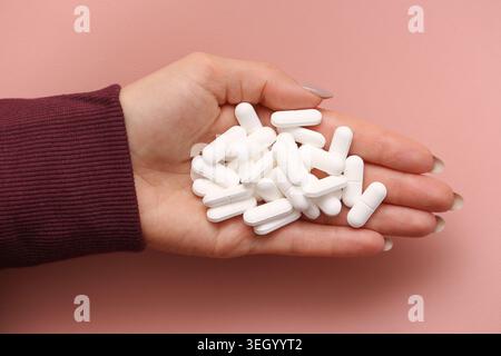 Woman holding white capsules in hand closeup. Pharmaceutical medication and healthcare treatment concept with medical supplements. Stock Photo