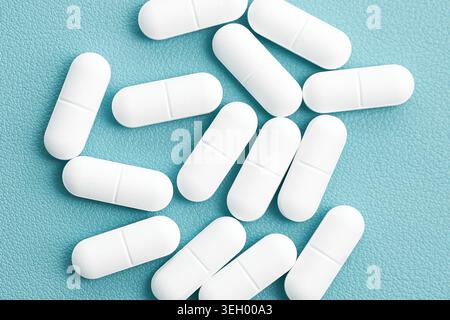 White capsules isolated on blue background closeup. Pharmaceutical medication and healthcare treatment concept with medical supplements. Stock Photo