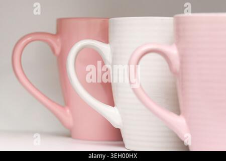 Pink ceramic mugs on shelf closeup. Minimal kitchen drinkware and modern home tableware concept with pastel colored cups indoors. Stock Photo
