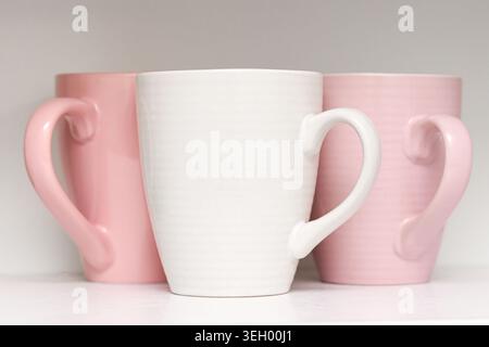 Pink ceramic mugs on shelf closeup. Minimal kitchen drinkware and modern home tableware concept with pastel colored cups indoors. Stock Photo