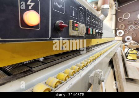 Edge bander machine automatically applies and trims edge banding material to wood panels, featuring a detailed control panel and conveyor belt in a bu Stock Photo