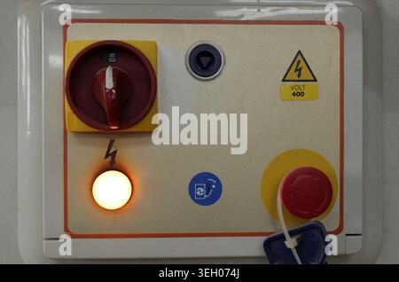 Industrial control panel close up with red locked emergency stop, main power switch on and glowing indicator light, highlighting machine safety and op Stock Photo