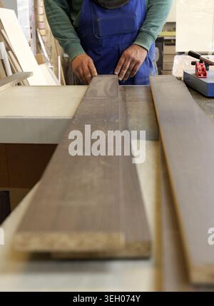 Carpenter's hands precisely position a wooden plank on a dusty workbench in a workshop, readying the lumber for measuring, cutting and detailed crafts Stock Photo