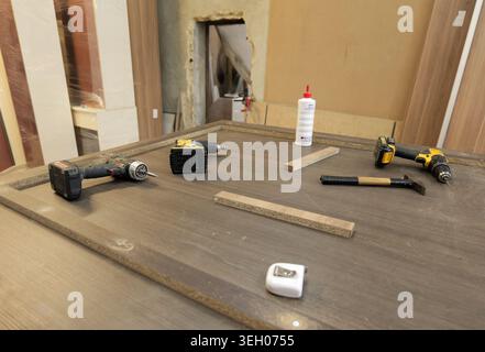 Drills, wood glue, and measuring tape are on a workshop workbench, depicting a scene of carpentry, assembly work, and furniture making using various h Stock Photo