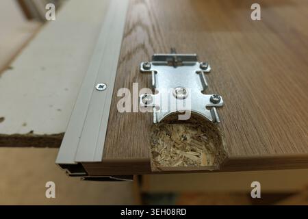 Furniture worker installing a hinge plate onto a particle board cabinet door, showing the screws and drilled hole for secure, long lasting assembly. 2 Stock Photo