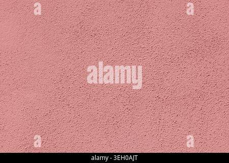 Close-up of a rustic, rough-textured stucco wall painted in a warm coral pastel pink hue, captured in Italy. This Mediterranean architectural surface Stock Photo