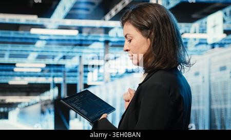 Data center programmer coding on tablet, optimizing equipment rigs using application. Close up of IT professional in server hub running programming script, adjusting system parameters Stock Photo