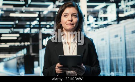 Smiling data center DevOps technician optimizing server load balancing using tablet app. Happy server hub employee worker adjusting system parameters on device to improve efficiency Stock Photo
