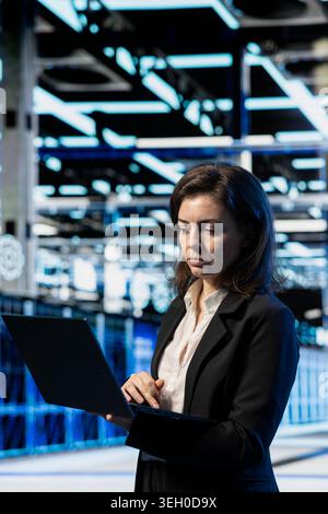 Data center system administrator using laptop software to do maintenance on mainframes. Server farm employee running checkup app on notebook to fix infrastructure machines malfunctions Stock Photo