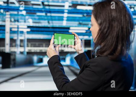 Green screen mockup smartphone used by server farm technician to film video. Data center employee recording footage with chroma key mobile phone, checking system diagnostics Stock Photo