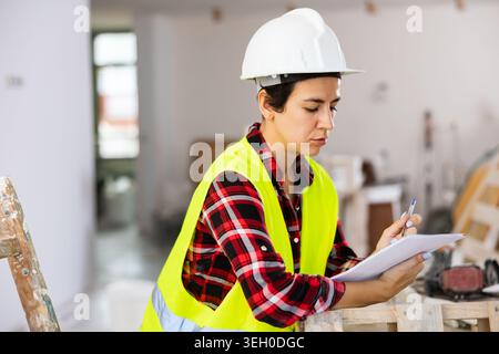 Female architect with papers in hands taking notes in building under renovation Stock Photo