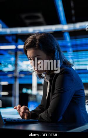 Writing code, laptop and female technician at desk in data center updating equipment network systems. Coding, upgrading supercomputers and woman in server room typing on notebook keyboard Stock Photo