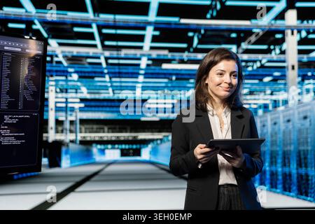 Smiling technician in data center using tablet to do digital twin scan of rigs to create wireframe virtualization. Happy IT expert doing electronics holographic overlay mapping in server hub Stock Photo
