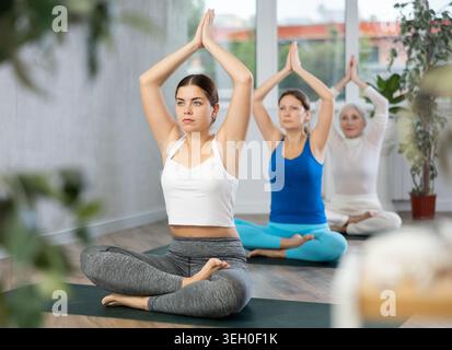 Active women practice pose sitting cross-legged with their arms raised Stock Photo