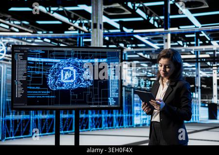 Data center software developer using AI projected on large display to troubleshoot backend operations equipment. Server farm employee running deep learning application on tablet, solving system bugs Stock Photo