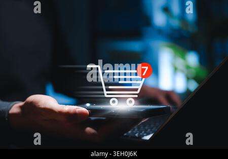 Online shopping cart and e-commerce purchase concept. Person using smartphone and laptop with cart icon, item notification, mobile checkout, digital Stock Photo