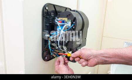 Electrical engineer installing an eco-friendly hand dryer in a commercial toilet facility using a screwdriver. Electrician wiring an environmentally f Stock Photo