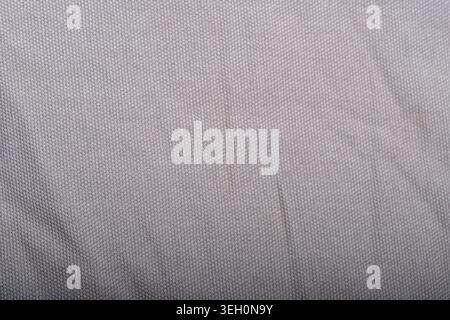 Close-up of gray woven fabric with fine threads and subtle vertical fold, useful as neutral textile background for design and interiors. Stock Photo