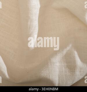 Natural beige linen fabric texture with visible woven fibers, soft folds, warm light and shadows for textile or lifestyle backgrounds. Stock Photo