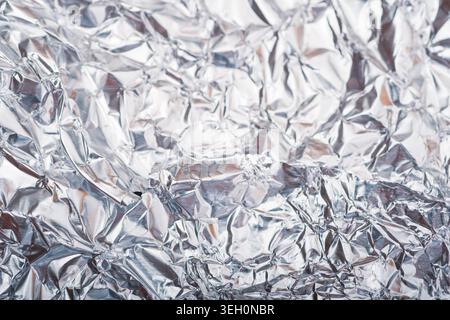 Detailed reflective aluminum foil background with dense silver folds, bright highlights and abstract crinkled metallic texture. Stock Photo