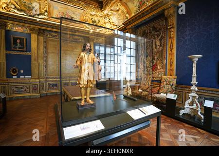An ornate gallery at the Musée Carnavalet displays a gilded statue of a violinist in a glass case surrounded by Baroque decor and tapestries. Stock Photo