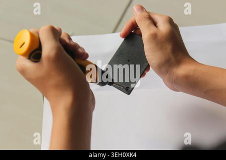 Close-up image of hands using an electric screwdriver to fasten screws on a black plastic electronic casing over a white background. Ideal for themes Stock Photo