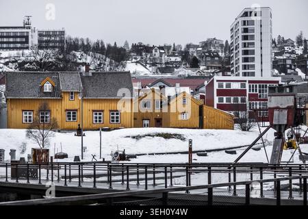 View of traditional yellow wooden houses nestled in a snowy landscape with modern architecture and hills in the background Tromso, Troms, Norway. Stock Photo