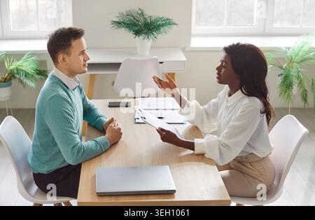 Female HR manager explaining job details to male candidate and answering questions during interview. Stock Photo
