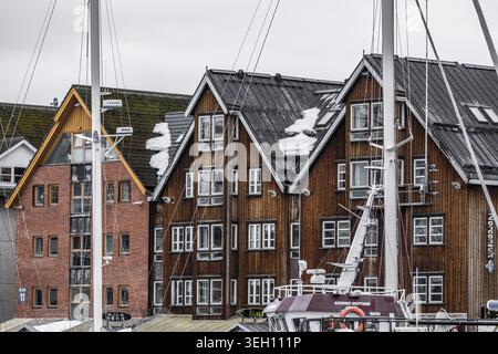 Tromso, Norway - 11 March 2026: View of traditional wooden waterfront buildings with snow on rooftops and sailboat masts in the harbor. Stock Photo