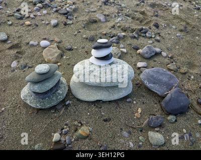 Zen stone pyramids and balanced pebbles on a sandy beach. Stock Photo