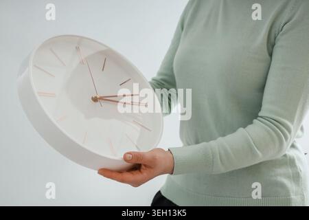 Woman setting time on wall clock on light background. Daylight saving time concept Stock Photo