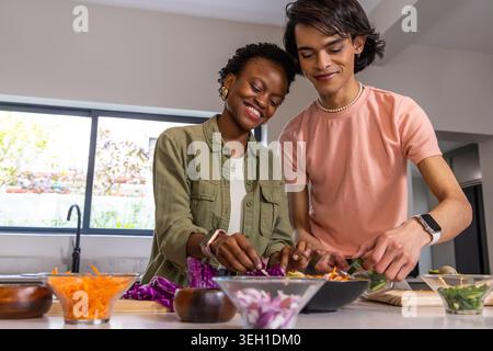 Couple with African American woman and Asian man preparing salad at kitchen island with glass bowls Stock Photo
