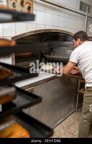 Baker placing fresh bread dough in hot oven Stock Photo