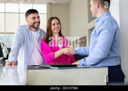 Smiling young couple shaking hands with car salesman at dealership desk Stock Photo