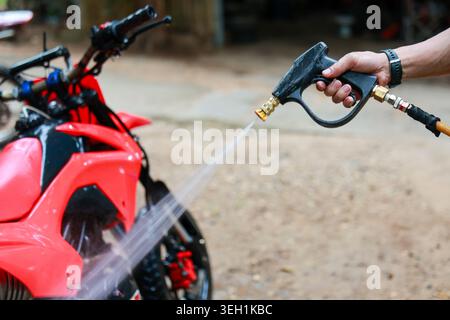 Man hand holding high pressure water spray gun diligently cleaning shiny red motorcycle. focused moment of vehicle maintenance and routine washing out Stock Photo
