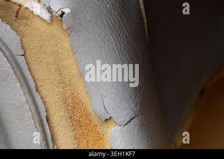 Close up view of torn old faux leather upholstery on seat. peeling damage reveals yellow foam underneath, showing signs of aging and wear and tear Stock Photo