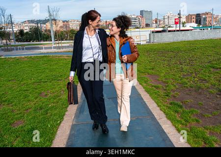 Two businesswomen walking together, discussing work, embracing partnership and support Stock Photo