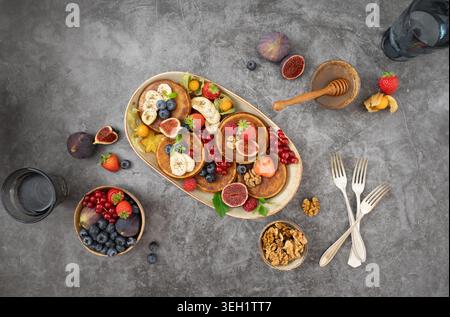Overhead breakfast composition with pancakes berries fruit bowls and honey on gray background Stock Photo