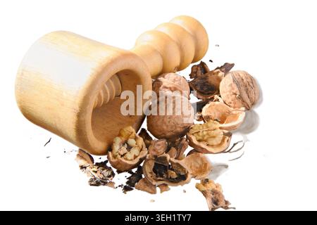 Handheld wooden nutcracker surrounded by cracked walnuts and scattered shells on white background, evoking rustic kitchen prep, natural ingredients an Stock Photo