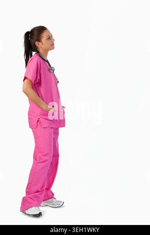 Adult woman standing in high-key studio wearing bright pink scrubs and stethoscope, copy space Stock Photo