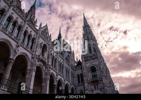 Hungarian parliament building, Budapest, showcasing detailed gothic revival architecture with prominent domes and spires under a dramatic, cloudy sunset sky, symbolizing history and politics Stock Photo