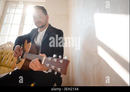 Handsome man playing guitar in the modern hotel room at sunny day Stock Photo