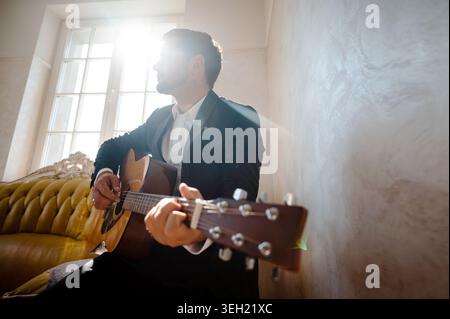 Handsome young man playing guitar in the living room at home Stock Photo